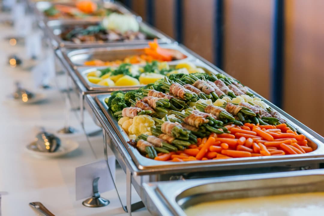 Buffet chafing trays with roasted vegetables and bacon-wrapped green beans