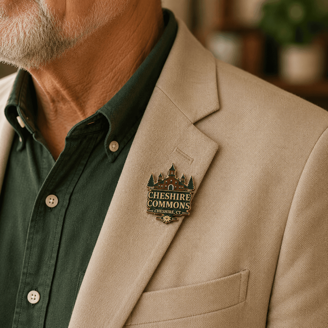 Gold hard enamel pin shaped like the Cheshire Commons building crest, worn on a jacket lapel