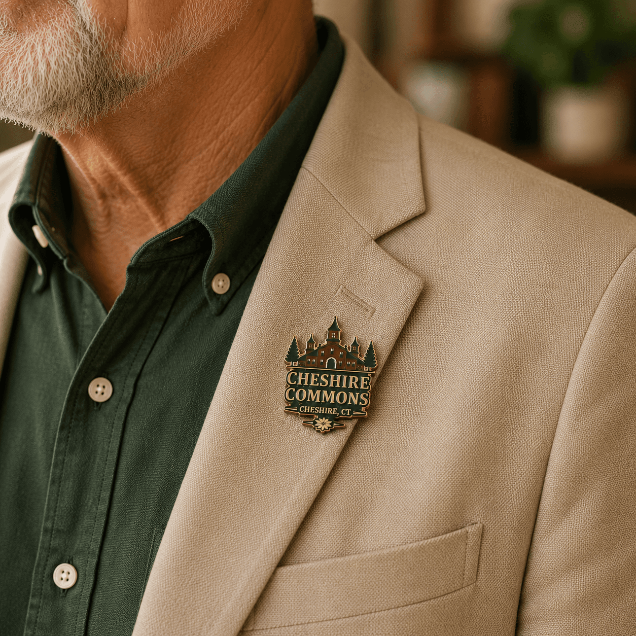 Gold hard enamel pin shaped like the Cheshire Commons building crest, worn on a jacket lapel