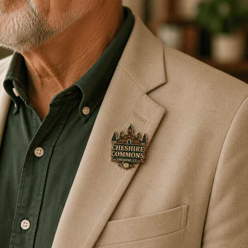 Gold hard enamel pin shaped like the Cheshire Commons building crest, worn on a jacket lapel