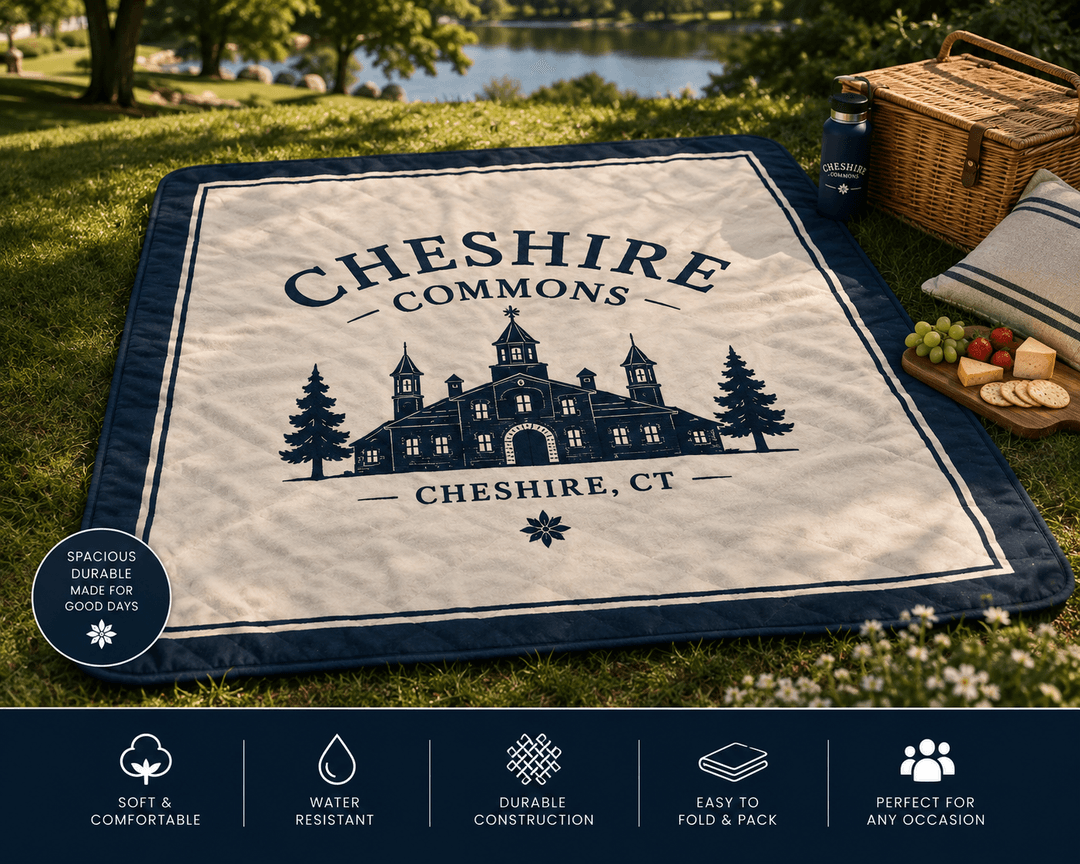 Navy quilted picnic blanket with the Cheshire Commons crest, laid out on the lawn
